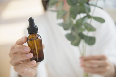 Woman holding bottle of essential oil and sprig of plant