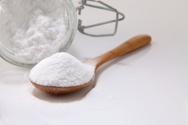 Close-Up Of Baking Soda In Wooden Spoon And Jar On White Background