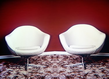 Two white chairs on rug, red background (video still)