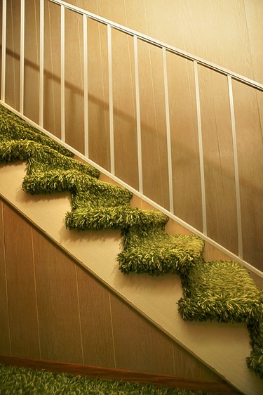 Stairs to the second floor with metal bannister and green shag carpet.
