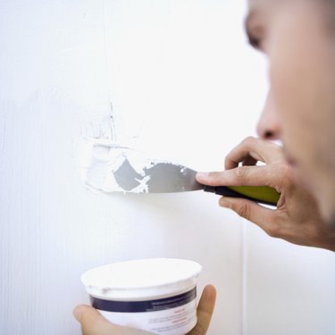 Close-up of a man applying filler to a wall with a putty knife