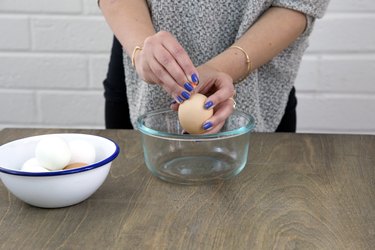 Holding egg over a bowl while piercing it with a pushpin.