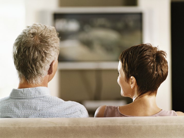 Rear View of a Mature Couple Sitting Side-By-Side on a Sofa Watching TV