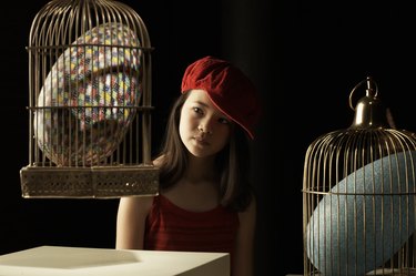 Girl (10-11) looking at giant colorful egg in cage